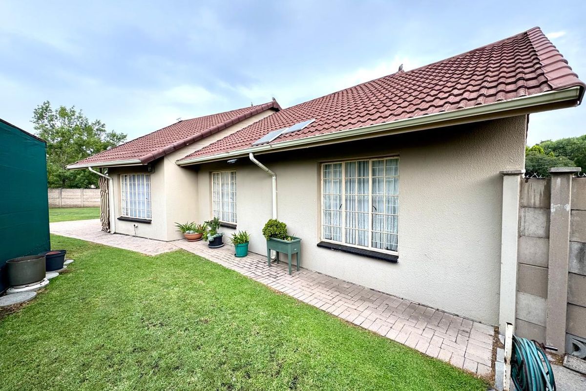 Rear view of the property featuring a tiled roof, paved walkway, and a well-maintained lawn area.
