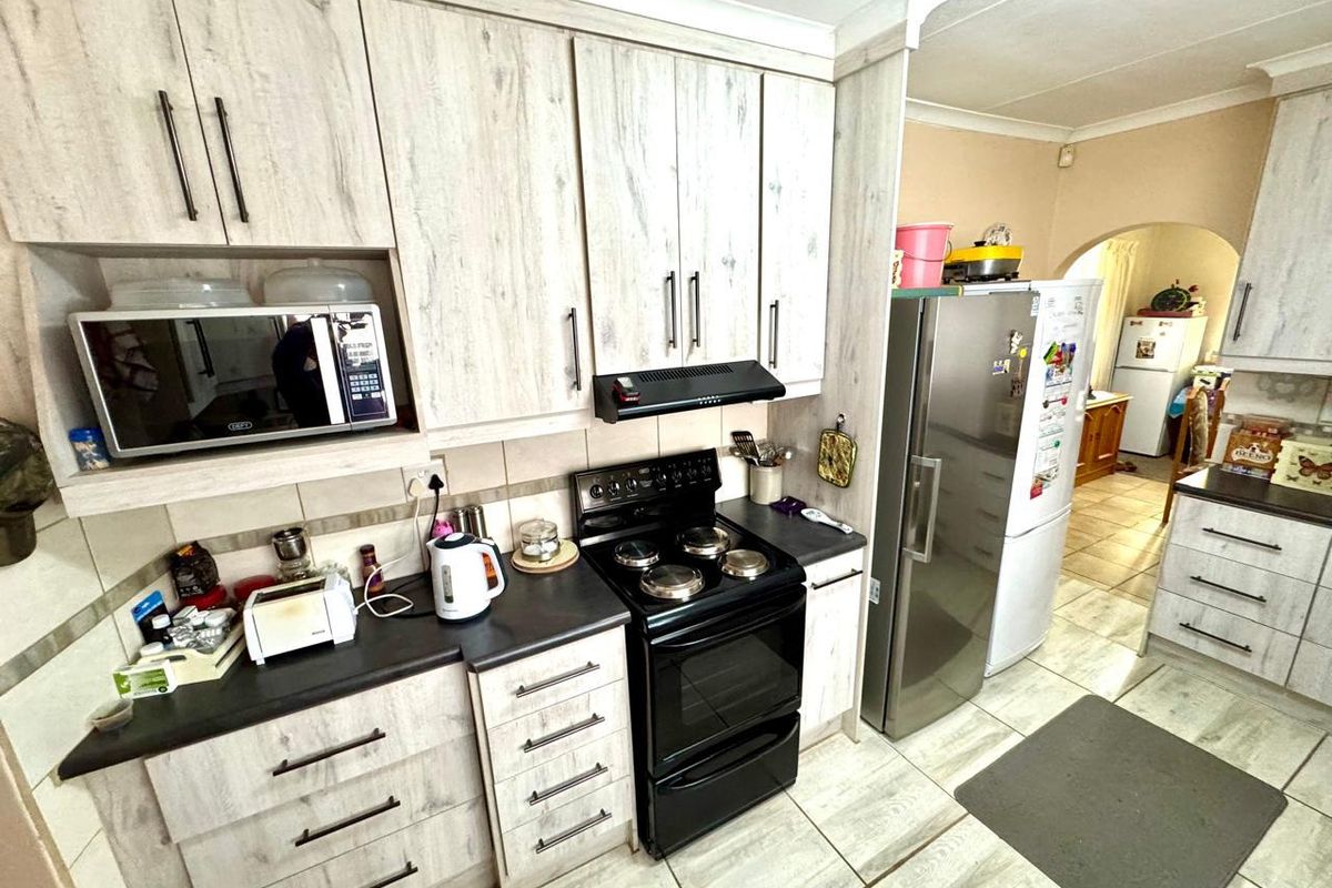 A functional kitchen featuring light wood-grain cabinetry, dark countertops, a built-in microwave, and a freestanding stove with an extractor fan.