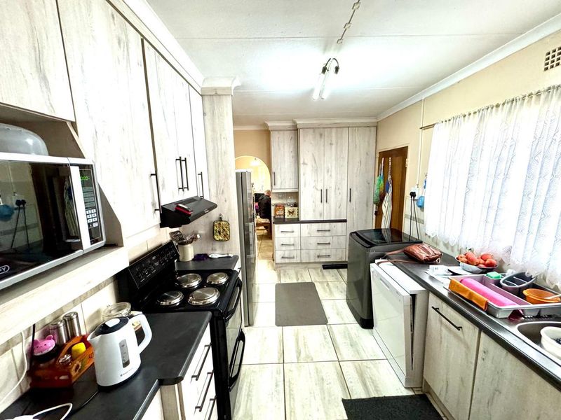 Functional kitchen featuring light wood-grain cabinetry, dark countertops, built-in oven with extractor fan, and dedicated space for laundry appliances.