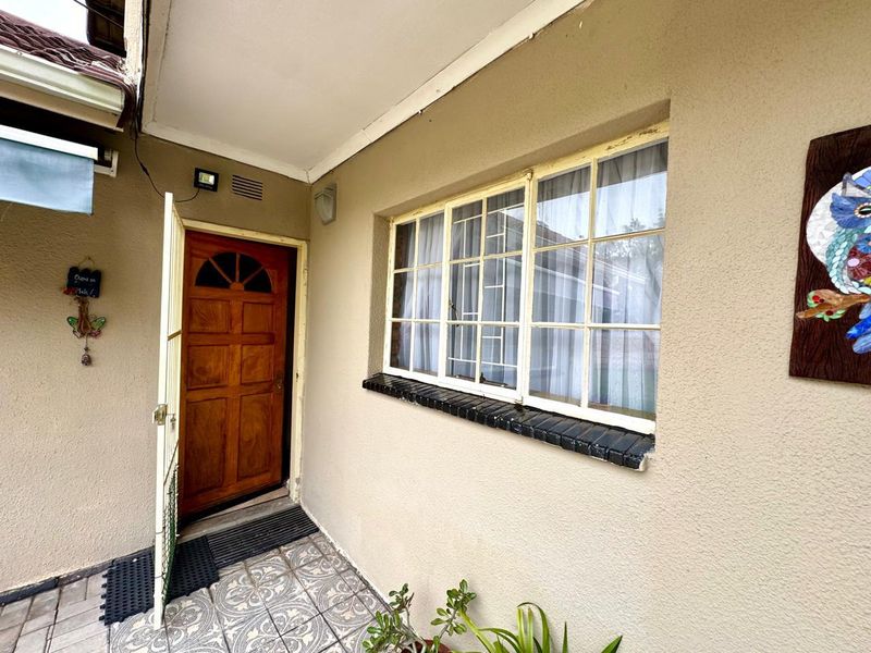 A covered entrance area featuring a wooden door, a multi-pane window with security bars, and patterned floor tiles.