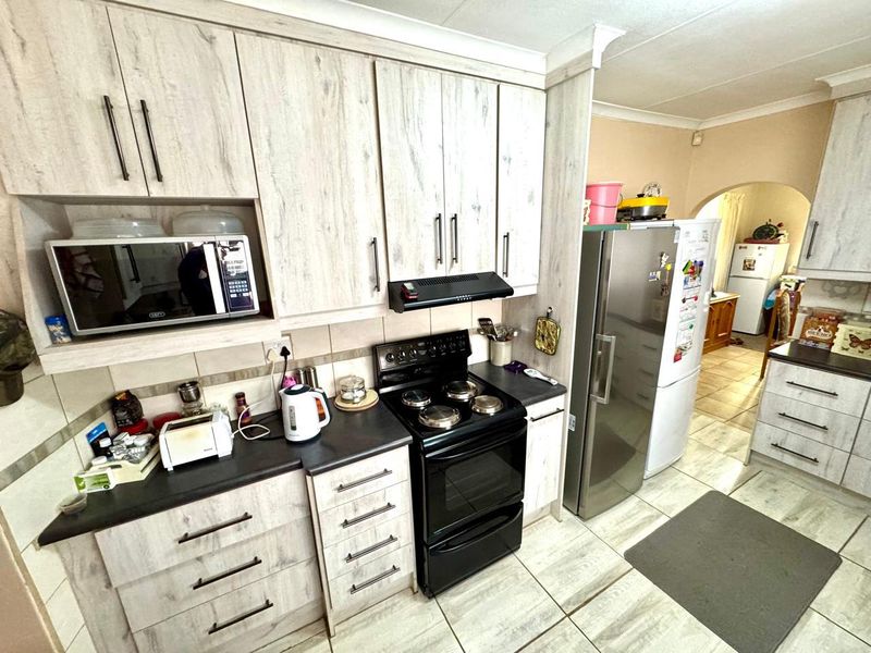 A functional kitchen featuring light wood-grain cabinetry, dark countertops, a built-in microwave, and a freestanding stove with an extractor fan.