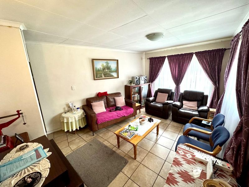A living room featuring tiled flooring and large windows with curtains, providing a functional and comfortable space for relaxation.