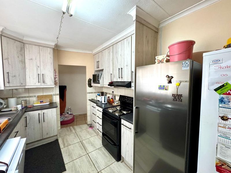 A functional kitchen featuring light wood-grain cabinetry, dark countertops, tiled flooring, and a built-in extractor fan with an adjacent utility area.