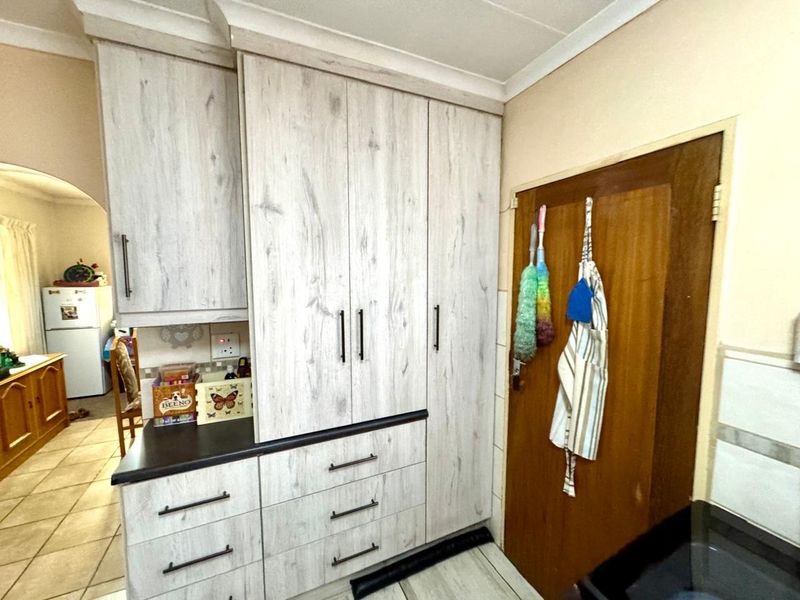 A functional kitchen area featuring light wood-grain cabinetry, dark countertops, and a classic wooden door leading to an adjacent space.