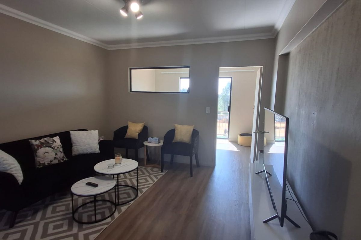 A well-maintained living room featuring laminate flooring, cove cornicing, and an internal window, providing a bright and functional living space.