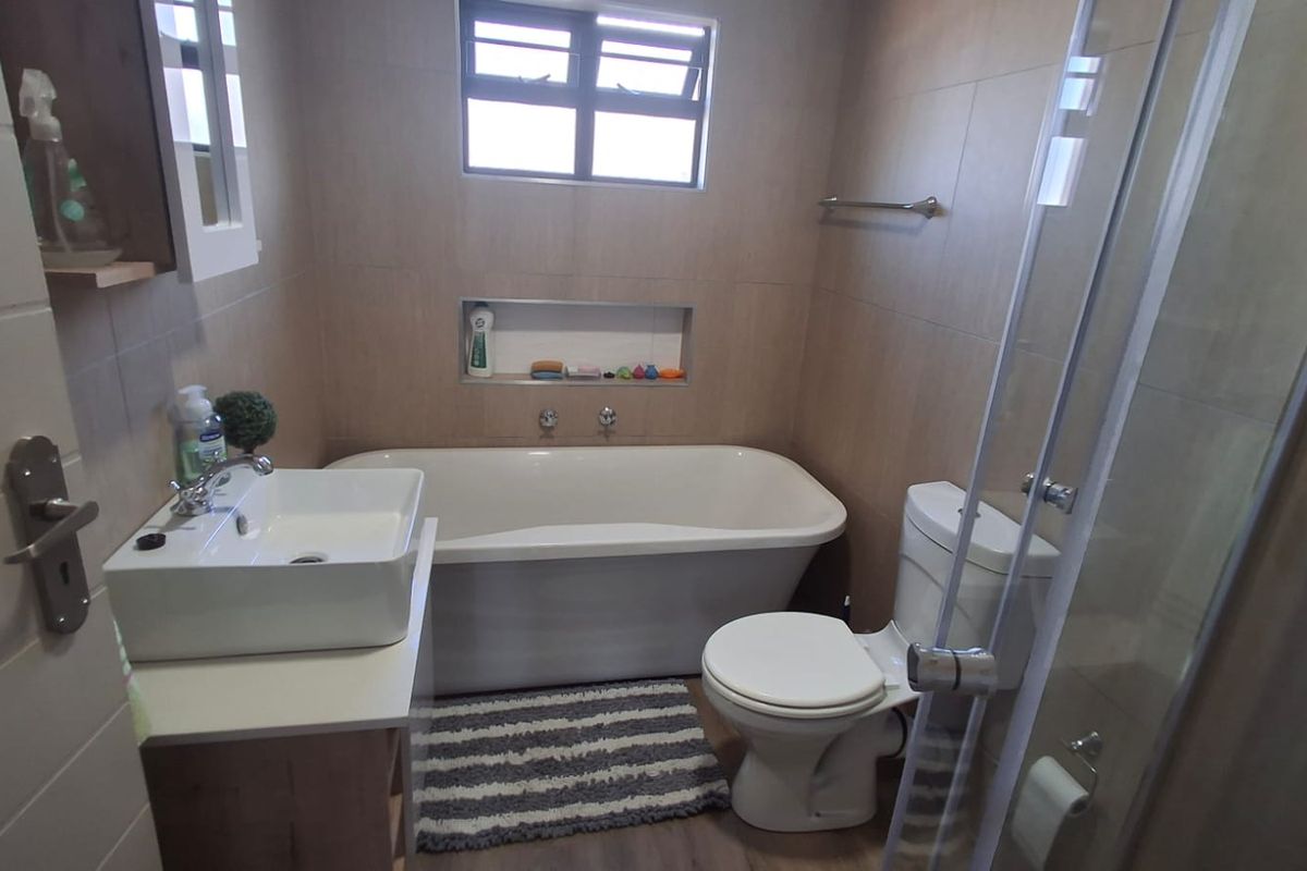 Modern bathroom featuring a freestanding bathtub, vessel sink vanity, glass-enclosed shower, and neutral wall tiling with a convenient recessed storage niche.