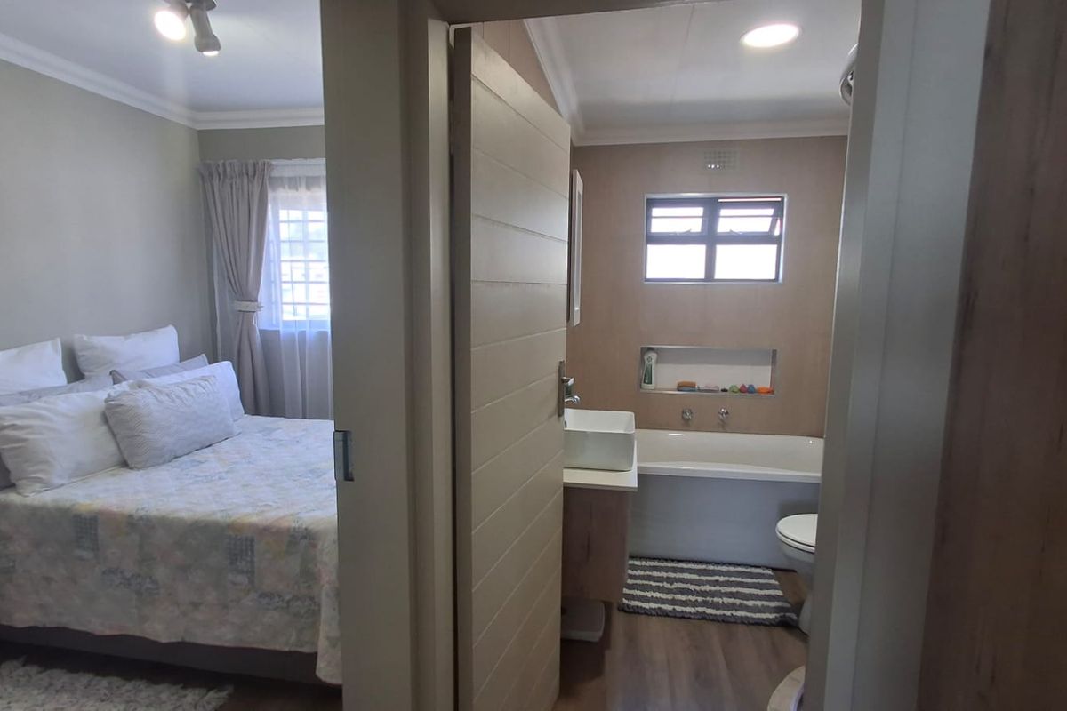 A bedroom featuring an en-suite bathroom with a bathtub, vessel sink, and modern vanity, finished with laminate flooring and recessed lighting.