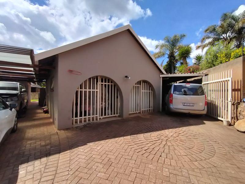 Front exterior view of the property featuring a paved driveway, arched security gates, and a covered carport area.