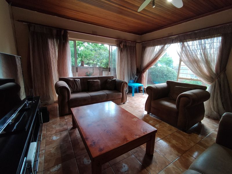 A living room featuring a timber ceiling, ceiling fan, and tiled flooring, with large sliding glass doors providing access to the outdoor area.