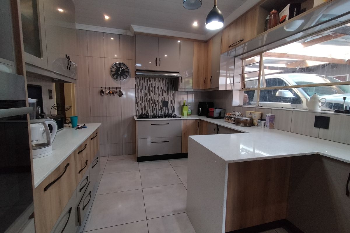 Modern kitchen featuring sleek cabinetry, quartz countertops, a gas hob with extractor fan, and tiled finishes throughout.