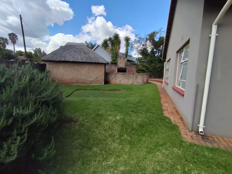 Rear garden area featuring a thatched lapa, built-in braai, and a brick paved pathway alongside the main house structure.