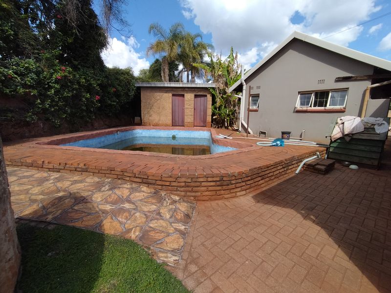 Outdoor pool area featuring brick paving, stone accents, and an adjacent outbuilding, requiring maintenance to the pool surface and surrounding structure.