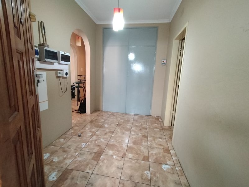 A functional hallway featuring tiled flooring, a built-in storage cupboard, and an arched entryway leading to adjacent living spaces.