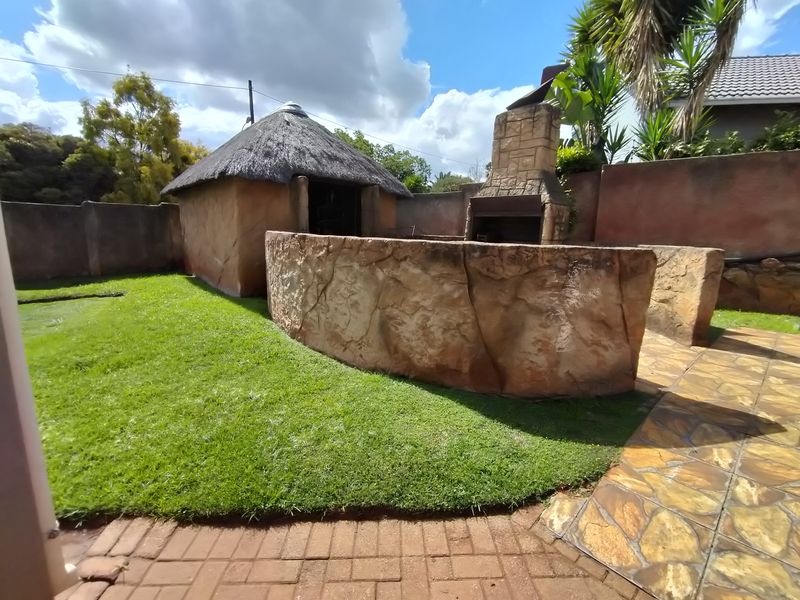 Rear garden area featuring a thatched lapa, built-in braai, stone-clad feature wall, and paved walkway.