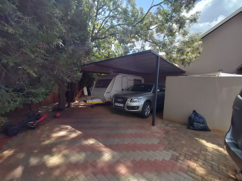 A paved rear exterior area featuring a functional metal carport structure, providing covered parking space alongside a boundary wall.