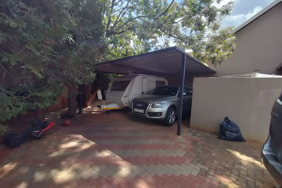 A paved rear exterior area featuring a functional metal carport structure, providing covered parking space alongside a boundary wall.