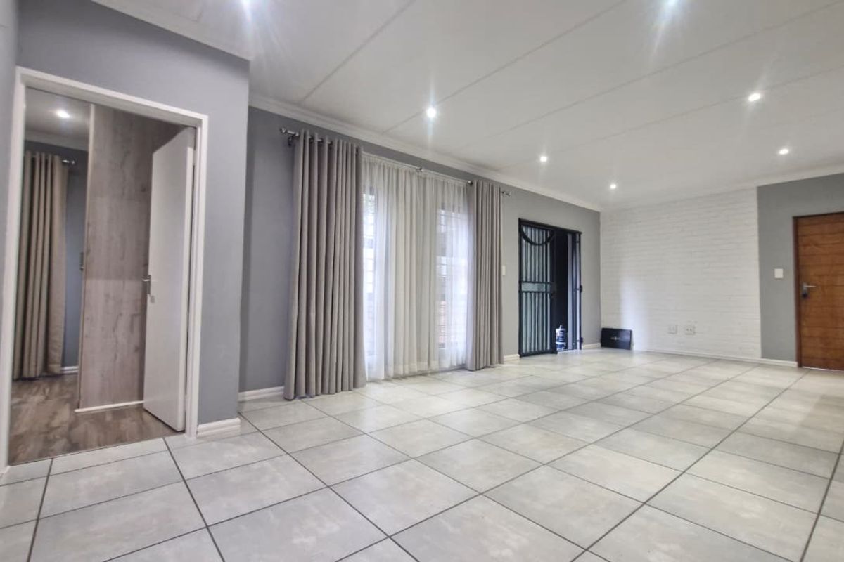 Spacious living area featuring neutral tiled flooring, recessed downlighting, and a textured brick feature wall, offering a bright and versatile open-plan space.