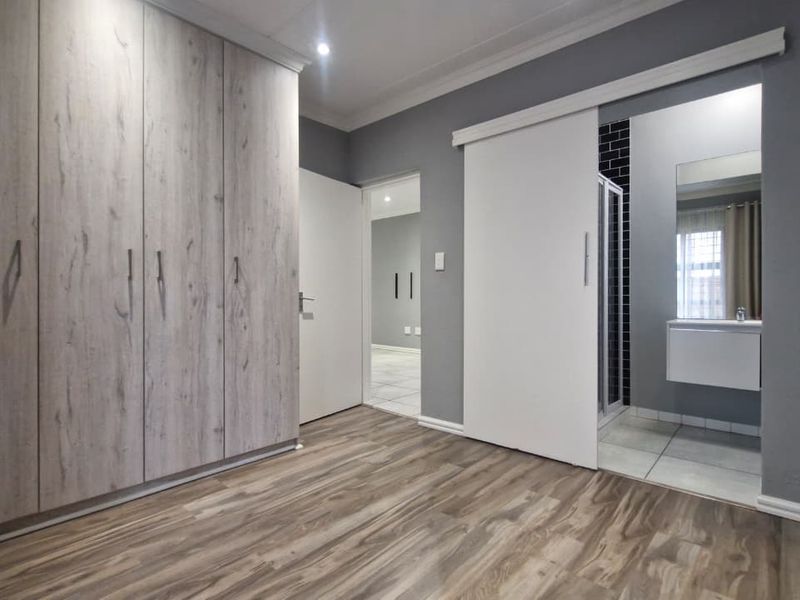 A modern bedroom featuring wood-look laminate flooring, extensive built-in cupboards, and a sliding door leading to an en-suite bathroom.