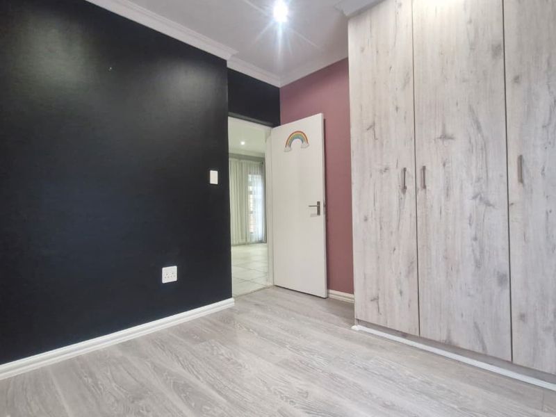 A clean bedroom featuring light wood-look laminate flooring, built-in cupboards, and a contrasting black feature wall.