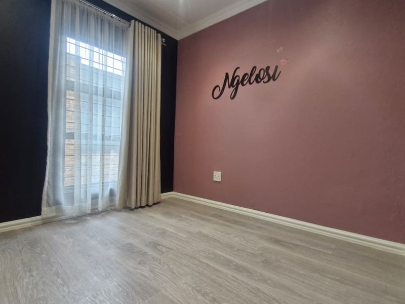 A clean, empty bedroom featuring light wood-look laminate flooring, neutral wall finishes, and window security bars.