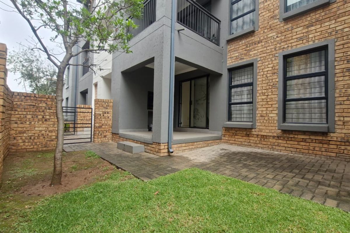Rear view of the apartment featuring a private garden, paved patio area, and a covered balcony with modern face brick and grey plaster finishes.