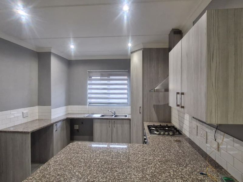 Modern kitchen featuring granite countertops, built-in cabinetry, a gas hob with extractor fan, and a double bowl sink with subway tile backsplash.