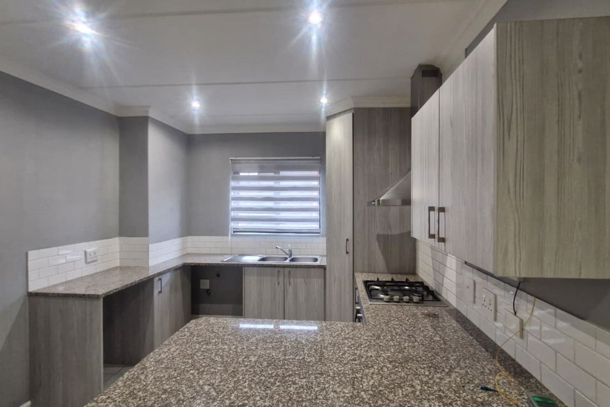 Modern kitchen featuring granite countertops, built-in cabinetry, a gas hob with extractor fan, and a double bowl sink with subway tile backsplash.