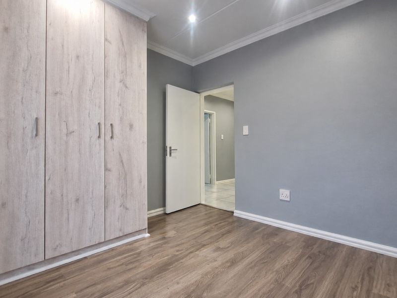 A clean, empty bedroom featuring modern light wood-grain built-in cupboards, grey walls, and durable laminate flooring with recessed ceiling lighting.