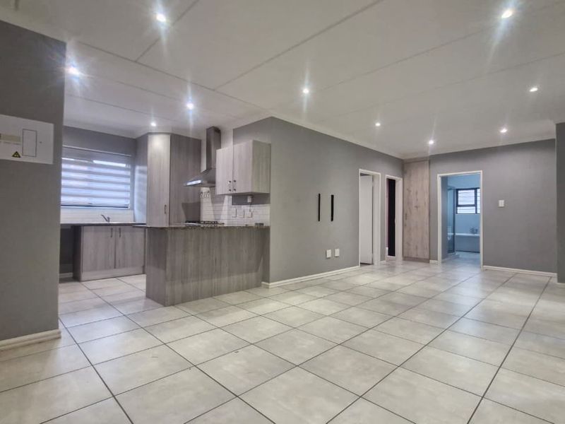 Spacious open-plan living area featuring a modern kitchen with built-in cabinetry, stone countertops, and a gas hob, finished with neutral tiled flooring throughout.