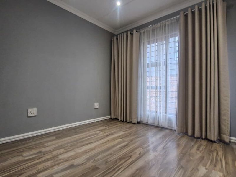 A bright, empty bedroom featuring modern laminate flooring, built-in cupboards, and a security gate leading to an outdoor area.