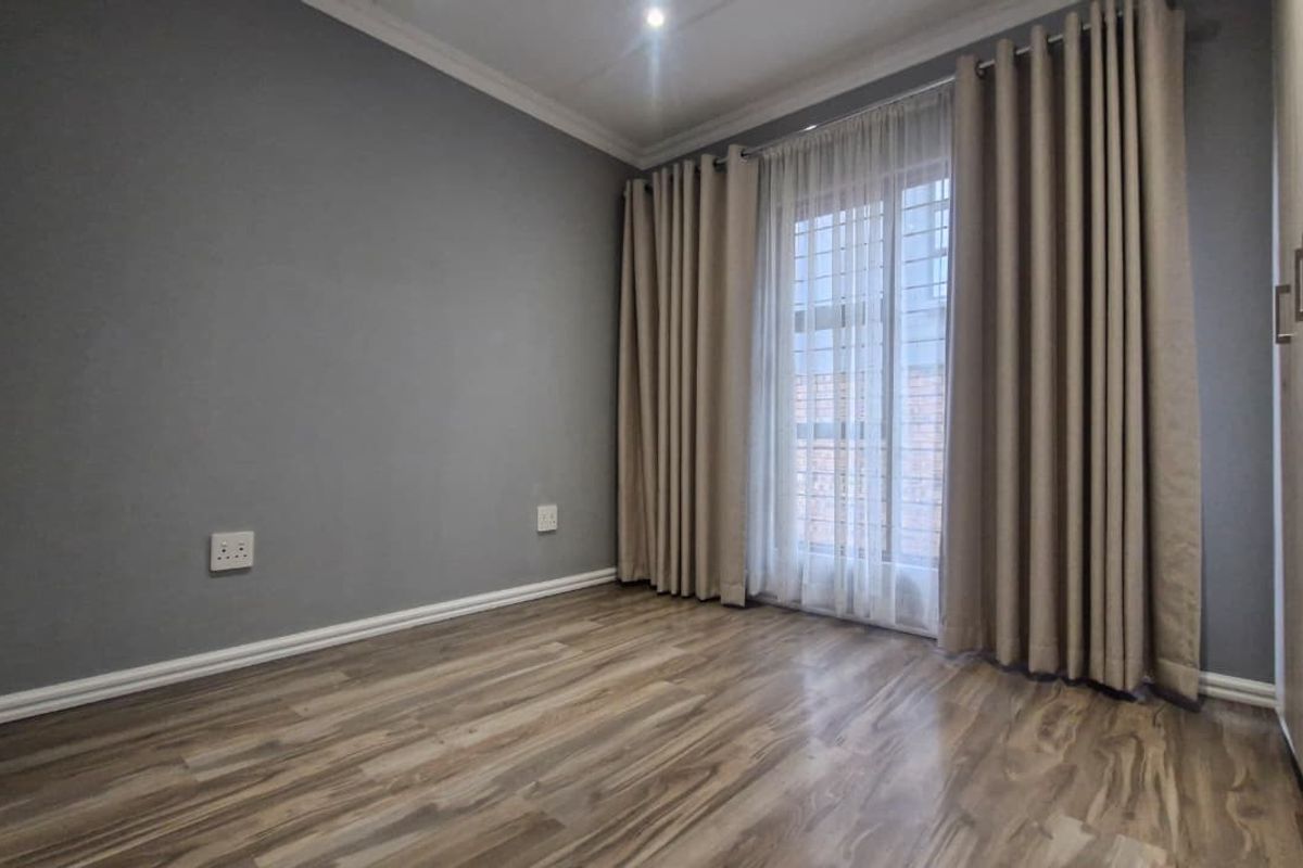 A bright, empty bedroom featuring modern laminate flooring, built-in cupboards, and a security gate leading to an outdoor area.
