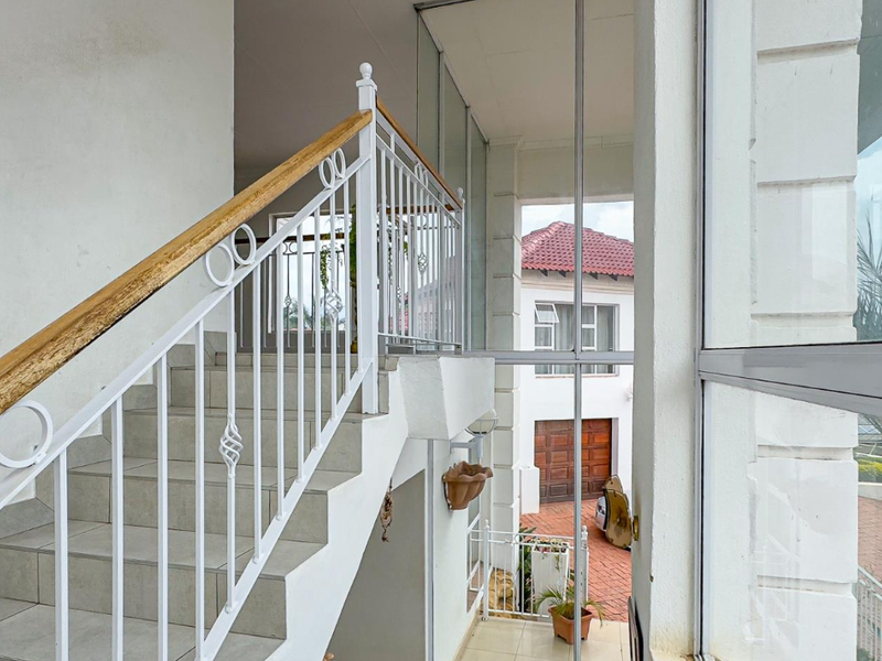 A bright, open-plan staircase area featuring a decorative wrought iron balustrade with a wooden handrail and large glass panels overlooking the exterior.