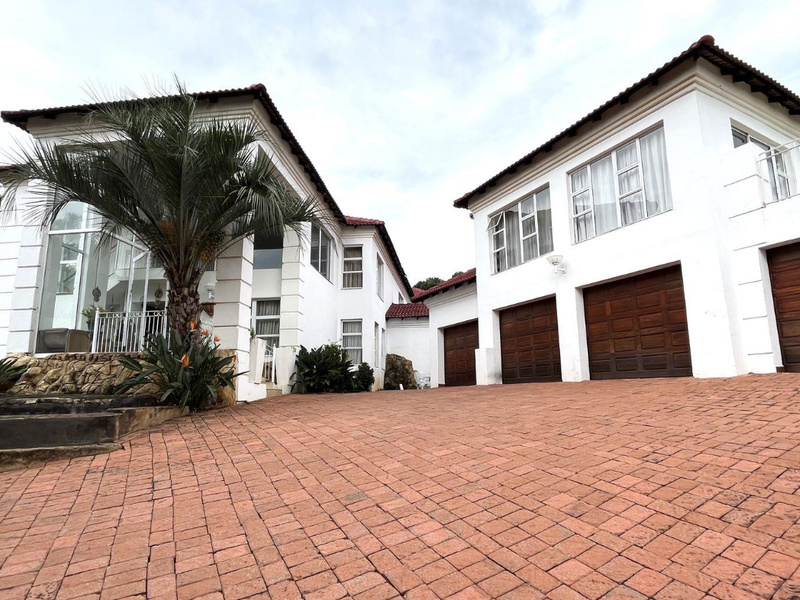 A spacious front exterior view featuring a large brick-paved driveway, multiple garage doors, and a multi-level white facade with stone accents.