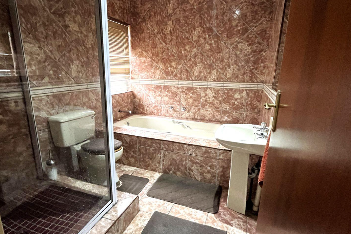 A dated bathroom featuring a built-in bathtub, separate shower enclosure, and pedestal basin with full-height marble-effect wall tiling.