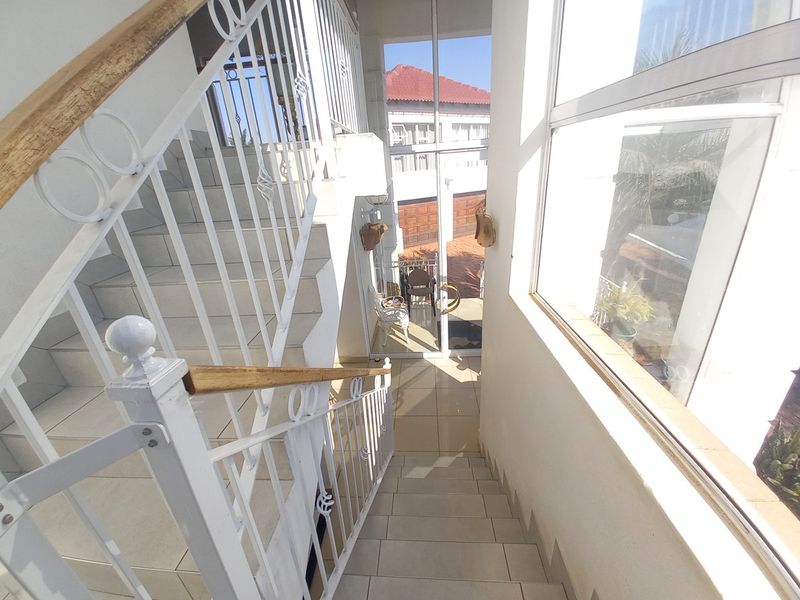 A bright, tiled staircase area featuring a white wrought iron balustrade with a wooden handrail and large windows providing natural light.
