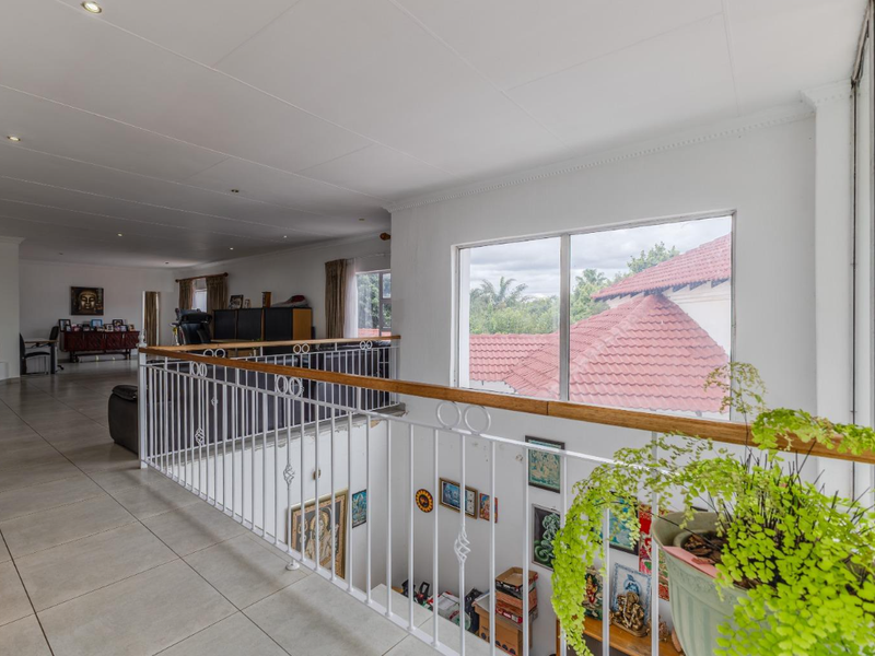 Spacious upper-level landing area featuring tiled flooring, a decorative metal balustrade with a wooden handrail, and large windows overlooking the property exterior.