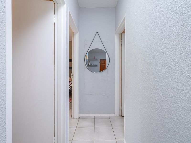 A narrow residential hallway featuring tiled flooring and textured walls, providing access to multiple rooms within the apartment.