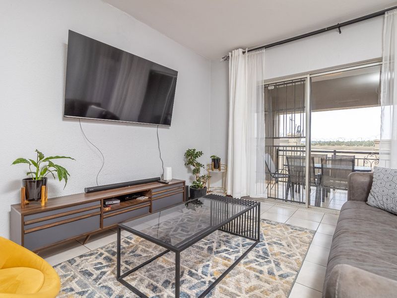 A bright living room featuring tiled flooring and a large sliding glass door that provides access to an outdoor balcony area.