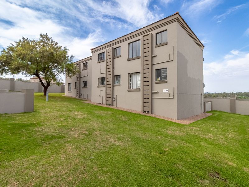 Rear view of a multi-story apartment building featuring a plastered facade, tiled roof, and surrounding communal lawn area.