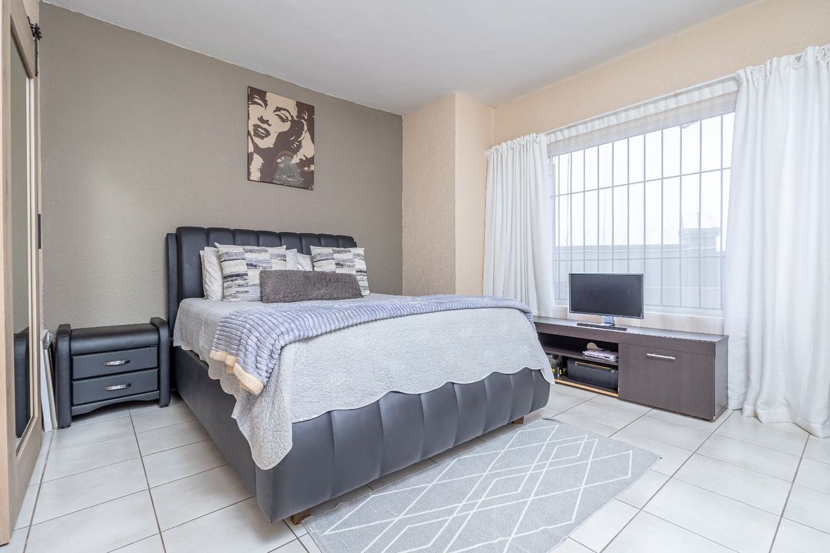 A well-lit bedroom featuring tiled flooring and a large window fitted with security bars, providing a functional and comfortable living space.