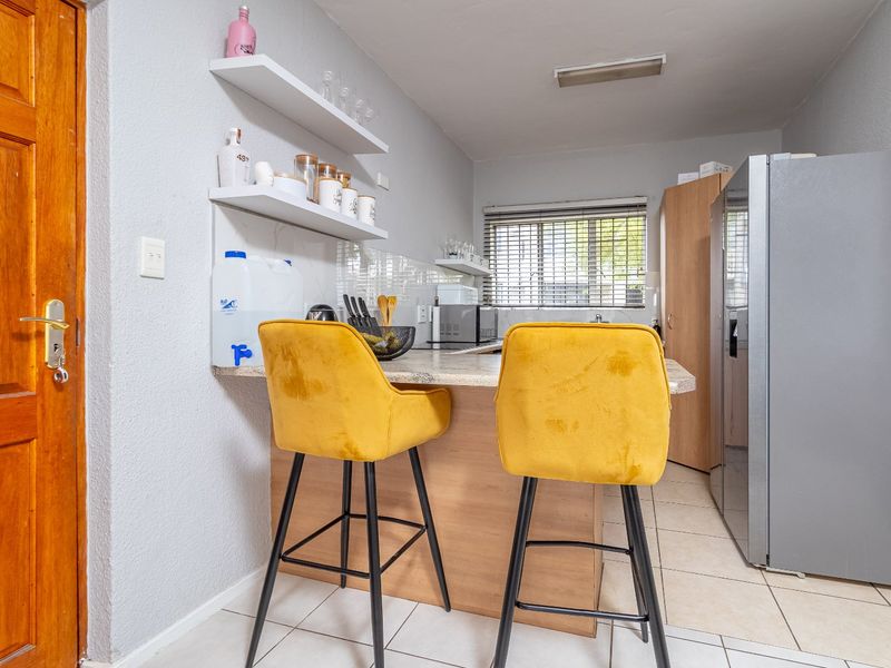 Compact kitchen featuring a breakfast bar, tiled flooring, floating shelving, and neutral cabinetry, providing a functional and efficient culinary space.