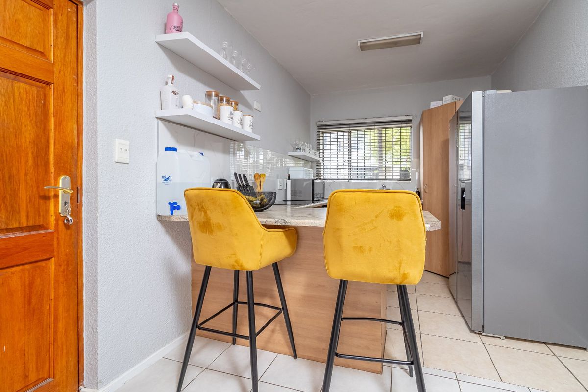 Compact kitchen featuring a breakfast bar, tiled flooring, floating shelving, and neutral cabinetry, providing a functional and efficient culinary space.