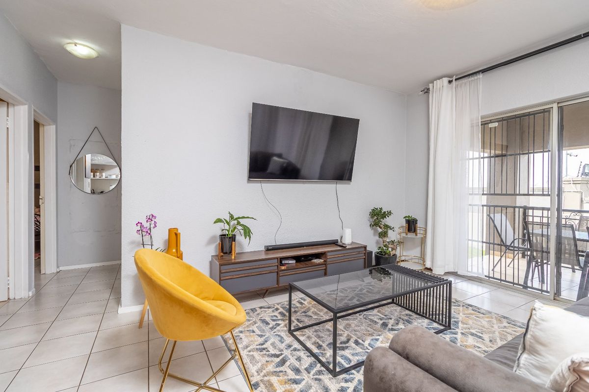 A bright living room featuring tiled flooring and a sliding glass door with security gate, providing access to an outdoor balcony area.