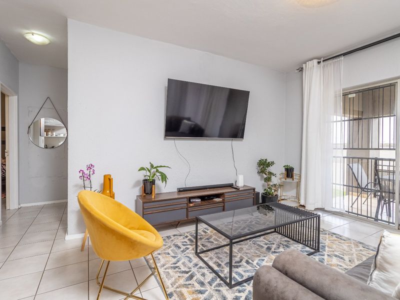 A bright living room featuring tiled flooring and a sliding glass door with security gate, providing access to an outdoor balcony area.