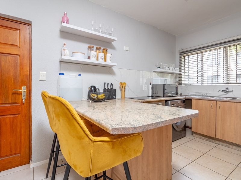 Functional kitchen featuring laminate countertops, built-in cabinetry, a stainless steel sink, and a marble-look splashback with convenient floating shelving.