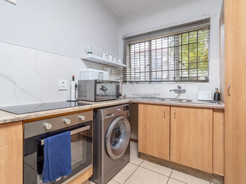 Compact kitchen featuring built-in oven, electric hob, stainless steel sink, and laminate cabinetry with marble-look splashback and tiled flooring.