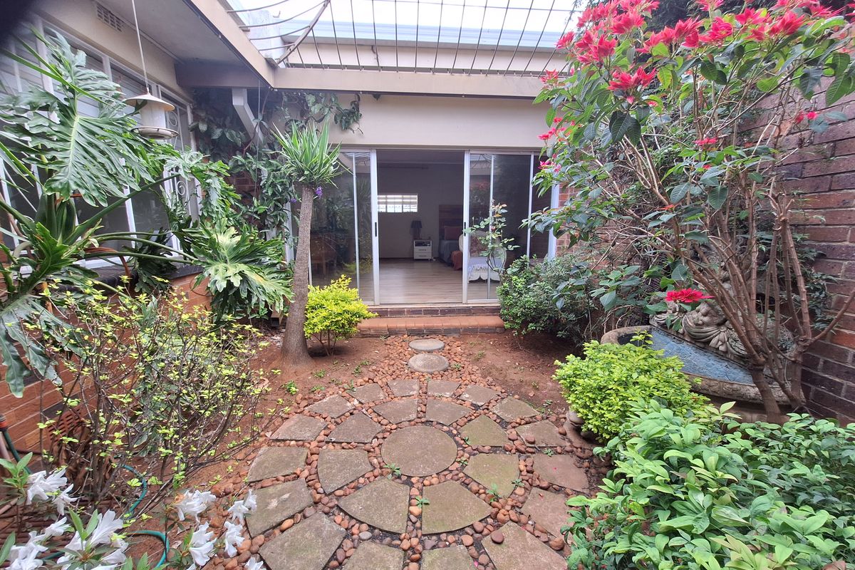 A private rear courtyard featuring a circular paved patio, established garden beds, and sliding glass door access to the interior living space.