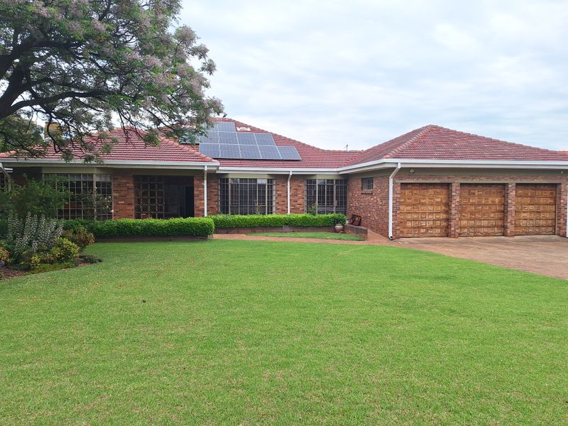 A well-maintained brick house featuring a triple garage, solar panels, and a spacious front lawn with established landscaping.