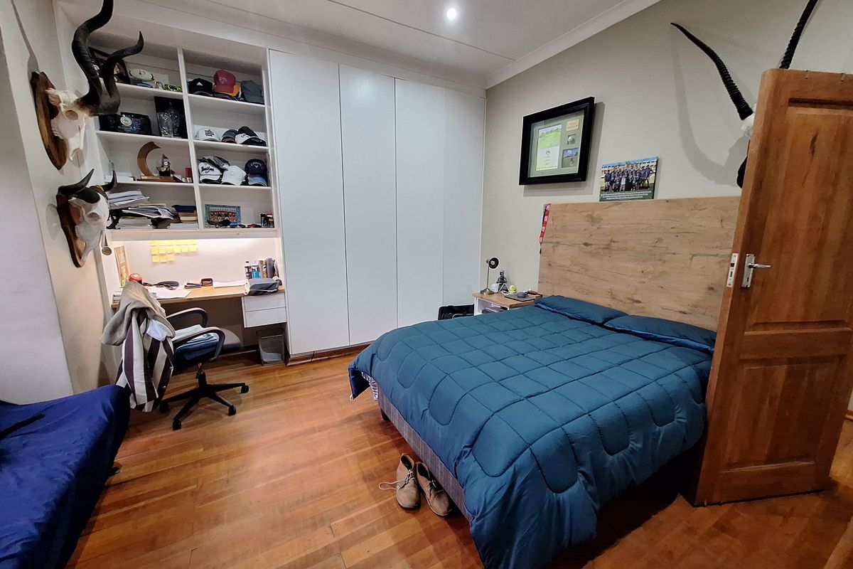 A well-maintained bedroom featuring polished wooden flooring, extensive built-in cabinetry with an integrated desk, and recessed ceiling lighting.