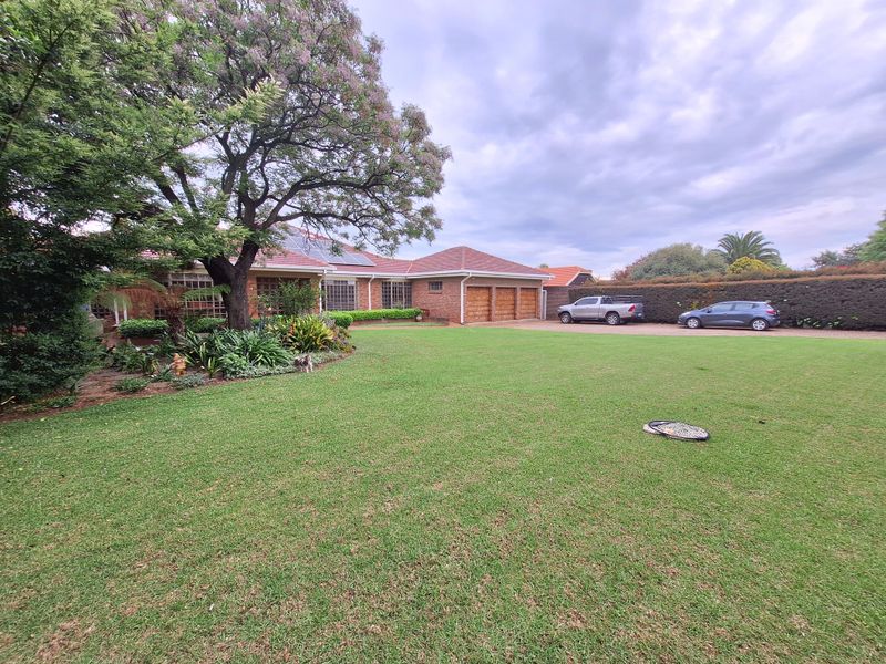 Spacious front exterior view featuring a large manicured lawn, mature tree, triple garage, and solar panels on a tiled roof.
